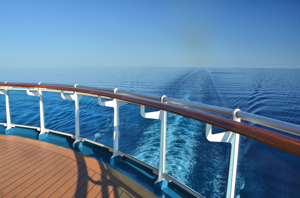 Blick über die Reling eines Kreuzfahrtschiffs auf das offene Meer. Die Kielspur des Schiffs zieht sich in die weite, blaue Ferne.